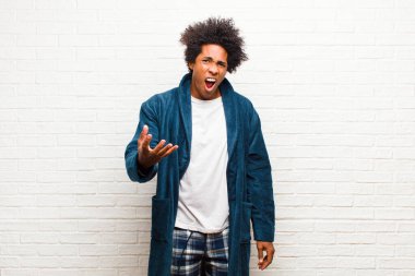 Genç siyahi adam pijama giyiyor. Önlüklü. Kızgın, sinirli ve sinirli görünüyor. 