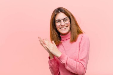 Genç ve güzel bir kadın kendini mutlu ve başarılı hissediyor. Gülümsüyor ve alkışlıyor. Pembe arka plana karşı alkışlarla tebrik ediyor.