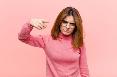 Genç, güzel bir kadın, kızgın agresif bir ifadeyle kameraya bakıyor. Pembe arka planda öfkeli, çılgın bir patron gibi görünüyor.