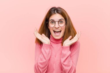 Genç ve güzel bir kadın pembe arka planda beklenmedik bir sürprizden dolayı şaşkın, heyecanlı, gülen, şaşkın ve mutlu hissediyor.