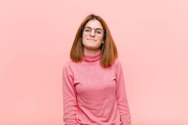 Genç ve güzel bir kadın neşeli ve gelişigüzel gülümsüyor. Pembe arka planda pozitif, mutlu, kendinden emin ve rahat bir ifadeyle.