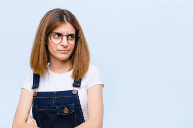 Genç, güzel bir kadın üzgün, üzgün ya da kızgın ve olumsuz bir tavır takınıyor, mavi arka plana karşı anlaşmazlık içinde.