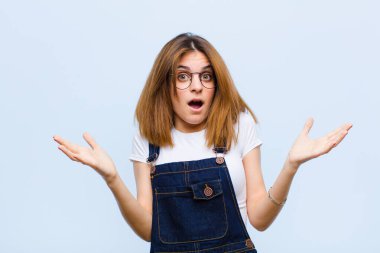 Genç ve güzel bir kadın son derece şok ve şaşırmış, endişeli ve paniklemiş hissediyor, stresli ve dehşete düşmüş bir bakışla mavi arka plana bakıyor.