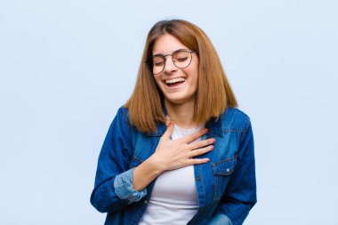 Genç ve güzel bir kadın komik bir şakaya yüksek sesle gülüyor, mutlu ve neşeli hissediyor, mavi arka planda eğleniyor.