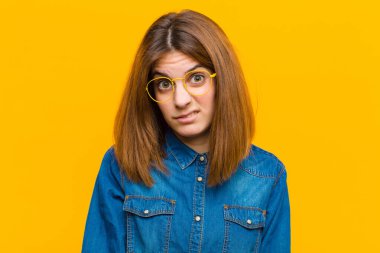 Genç ve güzel bir kadın şaşkın ve şaşkın hissediyor, aptal, afallamış bir ifadeyle beklenmedik bir şeye bakıyor sarı arka planda