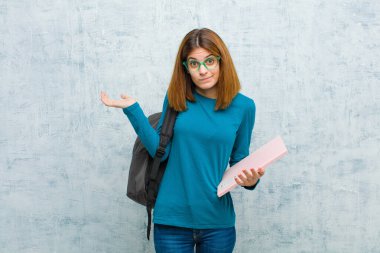 Genç bayan öğrenci şaşkın ve şaşkın hissediyor, şüpheci, farklı seçenekleri tartıyor ya da seçiyor grunge duvar arka planına karşı komik bir ifadeyle