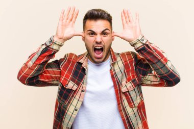 Panik ya da öfke içinde bağıran genç İspanyol adam, şok olmuş, korkmuş ya da öfkeli, elleri başının yanında izole edilmiş arka planda.