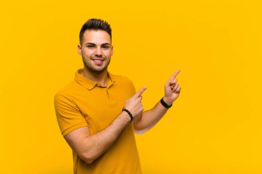 Genç İspanyol adam mutlu bir şekilde gülümsüyor ve her iki elinde fotokopi odasında turuncu duvara karşı nesne gösteriyor.