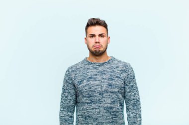 Genç İspanyol bir adam üzgün ve stresli. Kötü bir sürpriz yüzünden üzgün. Mavi arka plana karşı olumsuz ve endişeli bir bakış.