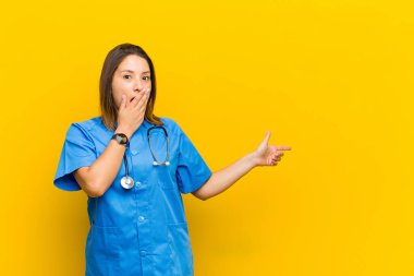 Mutlu, şaşkın ve şaşırmış hissediyorum, elimle ağzımı kapatıyorum ve sarı duvara yapıştırdığım yanal fotokopi alanını işaret ediyorum.