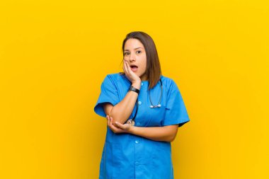 Şok ve inançsızlıkla ağzı açık, elleri yanakları ve kolları çapraz, sarı duvara karşı sersemlemiş ve şaşırmış hissediyordu.