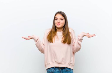 Genç, güzel bir kadın şaşkın ve şaşkın, şüpheci, farklı seçenekleri tartıyor ya da beyaz arka plana karşı komik bir ifadeyle seçiyor.