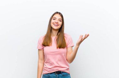 Genç, güzel bir kadın kendini mutlu, şaşırmış ve neşeli hissediyor. Pozitif bir tavırla gülümsüyor. Beyaz arka plana karşı bir çözüm ya da fikir buluyor.