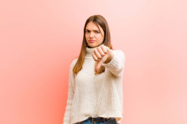 Genç, güzel bir kadın kızgın, sinirli, hayal kırıklığına uğramış ya da hayal kırıklığına uğramış, pembe arka plana ciddi bir bakışla karşı karşıya.