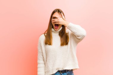 Genç, güzel bir kadın şok olmuş, korkmuş ya da korkmuş görünüyor. Yüzü elle örtülmüş ve parmaklarının arasından pembe arka plana bakıyor.