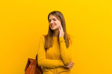 Genç, güzel bir kadın, yanağını tutuyor ve ağrılı diş ağrısı çekiyor. Hasta, sefil ve mutsuz hissediyor. Turuncu arka planda dişçi arıyor.