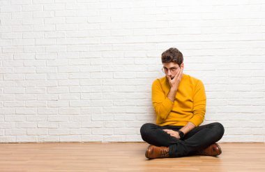 Genç yakışıklı adam tuğla duvar dokusuna karşı evde oturuyor.