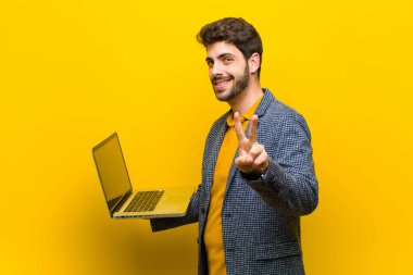 Bilgisayarı turuncu arka planda olan genç ve yakışıklı bir adam.