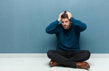 Genç, yakışıklı bir adam yerde oturmuş stresli ve hayal kırıklığına uğramış hissediyor. Yumruklarını havaya kaldırıyor. Yorgun, mutsuz ve migren ağrısı çekiyor.