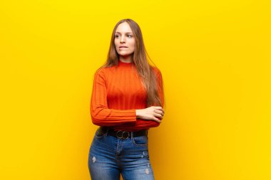 Genç, güzel bir kadın şüphe ediyor ya da düşünüyor, dudağını ısırıyor ve gergin hissediyor, turuncu arka plandaki boşluğu kopyalamak istiyor.