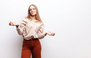 Şaşkın, kafası karışmış ve stresli görünen genç bir kadın, farklı seçenekler arasında merak ediyor, beyaz duvara karşı kararsız hissediyor.