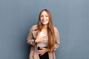 Genç ve güzel bir kadın komik bir şakaya yüksek sesle gülüyor, mutlu ve neşeli hissediyor, gri arka planda eğleniyor.