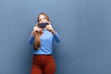 young pretty woman using a smart phone against blue wall with a copy space