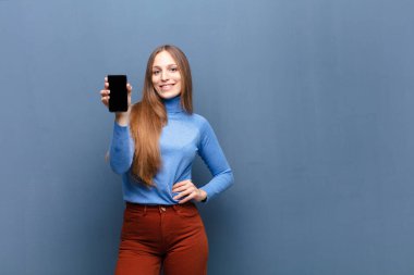 young pretty woman using a smart phone against blue wall with a copy space