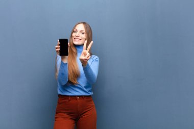 young pretty woman using a smart phone against blue wall with a copy space