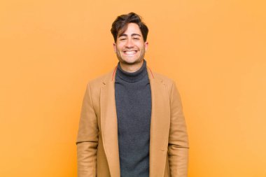 Genç yakışıklı adam mutlu ve şapşal görünüyor. Geniş, eğlenceli, deli gülüşü ve gözleri turuncu arka planda açık.