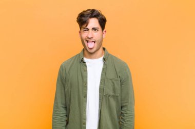 Genç yakışıklı adam iğreniyor ve rahatsız oluyor. Dilini dışarı çıkarıyor. Çirkin ve turuncu arka planda iğrenç bir şeyden hoşlanmıyor.