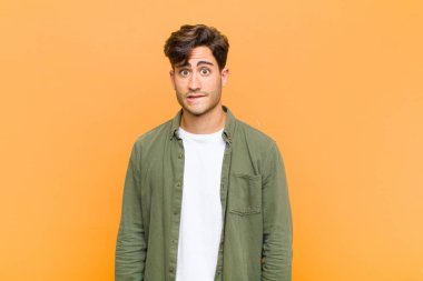 Genç yakışıklı adam kendini cahil, kafası karışmış ve hangi seçeneği seçeceğine karar verememiş turuncu arka plandaki sorunu çözmeye çalışıyor.