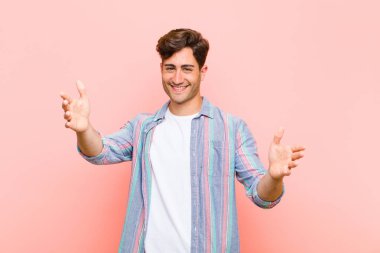 Genç yakışıklı adam neşeyle gülümsüyor sıcak, dostça, sevgi dolu bir kucaklama yapıyor, pembe arka planda mutlu ve sevimli hissediyor.