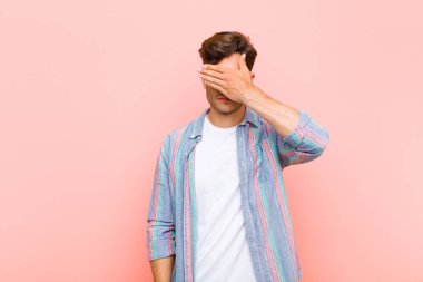 Genç ve yakışıklı bir adam gözlerini kapatıyor. Bir eli korkmuş ya da endişeli, merak ediyor ya da körü körüne pembe arka plana karşı bir sürpriz bekliyor.