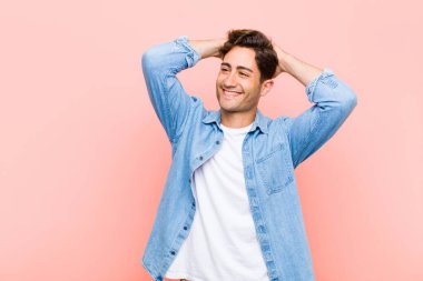 Genç yakışıklı adam gülümsüyor ve rahatlıyor, tatmin oluyor ve kaygısızca gülüyor, pembe arka plana gülüyor.