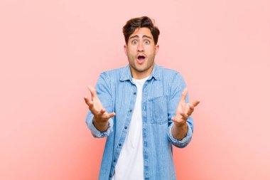 Genç yakışıklı adam açık sözlü ve şaşkın, şaşkın ve şaşkın pembe arka plana karşı inanılmaz bir sürpriz ile