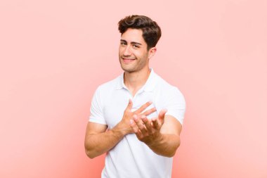 Genç yakışıklı bir adam mutlu ve aşık, bir eli kalbinin yanında gülümsüyor ve diğeri de pembe arka planda uzanıyor.