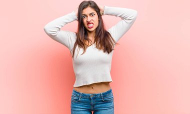 Genç, güzel bir kadın kendini stresli, endişeli, endişeli ya da korkmuş hissediyor. Elleri başının üstünde, pembe arka planda hata yaparken panikliyor..