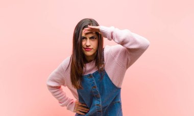 Genç, güzel bir kadın şaşkınlık ve şaşkınlık içinde bakıyor. Alnı açık, uzaklara bakıyor. Pembe arka planı izliyor ya da araştırıyor..