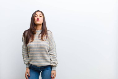 Genç, güzel bir kadın tatlı, eğlenceli, mutlu, sevimli bir yüz ifadesiyle dudaklarını birbirine bastırıyor ve beyaz duvara yapışmış bir öpücük yolluyor.