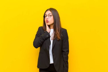 Genç, güzel bir kadın şok olmuş ve şok olmuş hissediyor. Ağzı açık bir şekilde turuncu duvara dayanmış, yüz yüze inanamıyor.