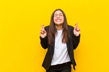 Genç ve güzel bir kadın gergin ve umutlu, dua ediyor ve turuncu duvara karşı iyi şanslar diliyor.