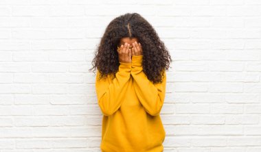 Genç siyahi kadın üzgün, hayal kırıklığına uğramış, gergin ve depresif, iki eliyle yüzünü örten, tuğla duvara karşı ağlayan