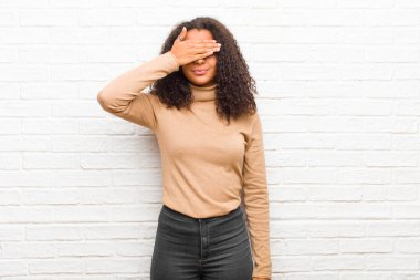 Genç siyah kadın gözlerini kapatıyor tek eliyle. Korkmuş ya da endişeli, merak ediyor ya da körü körüne tuğladan duvara karşı bir sürpriz bekliyor.