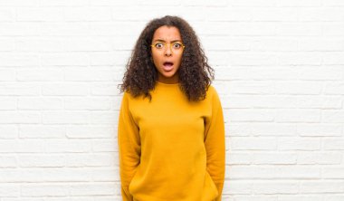 Genç siyahi kadın korkmuş ve şok olmuş hissediyor, ağzı ardına kadar açık tuğla duvara karşı şaşkınlık içinde.