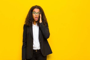 Siyahi iş kadını şaşırmış, ağzı açık, şok olmuş, turuncu duvara karşı yeni bir düşünce, fikir ya da konsept keşfediyor.