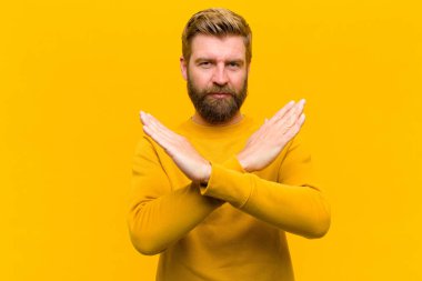 Genç sarışın adam senin bu tavırlarından rahatsız ve bıkkın görünüyor, yeter artık! Eller önde çapraz, turuncu duvara yaslanmanı söylüyor.