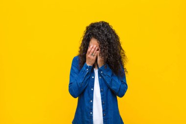 Genç, güzel bir kadın üzgün, hayal kırıklığına uğramış, gergin ve depresif, iki eliyle yüzünü kapatmış, turuncu duvara karşı ağlıyor.