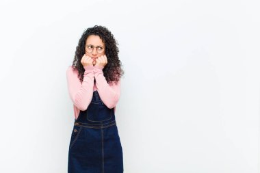 Genç, güzel bir kadın endişeli, gergin, stresli ve korkmuş görünüyor. Tırnaklarını yiyor ve beyaz duvara karşı yanal kopyalama alanı arıyor.