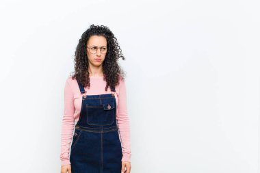 Genç, güzel bir kadın üzgün, üzgün ya da kızgın ve olumsuz bir tavır takınıyor, beyaz duvara karşı anlaşmazlık içinde.